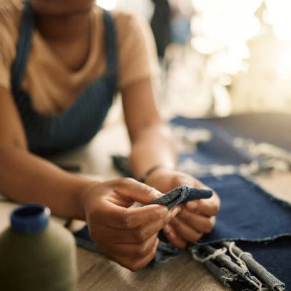 Fashion design student sewing, learning and making creative denim clothes in a clothing manufacturing factory. Industry, artistic and fashionable designer busy in a workshop working on stylish jeans